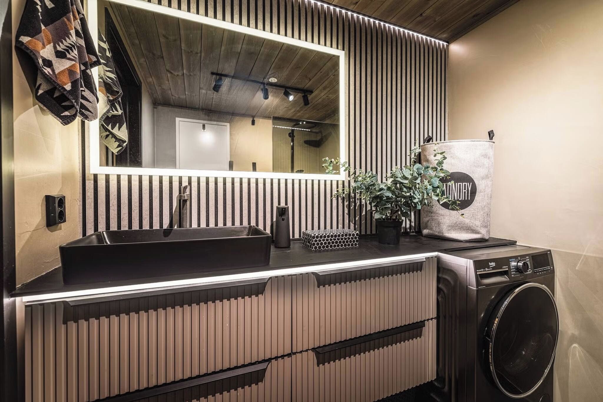 A modern bathroom with a black sink, a mirror, a washing machine, and a potted plant.