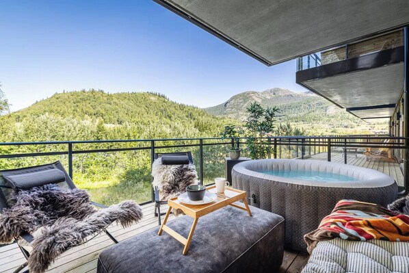 A balcony with a hot tub, seating, and a view of a mountainous landscape.