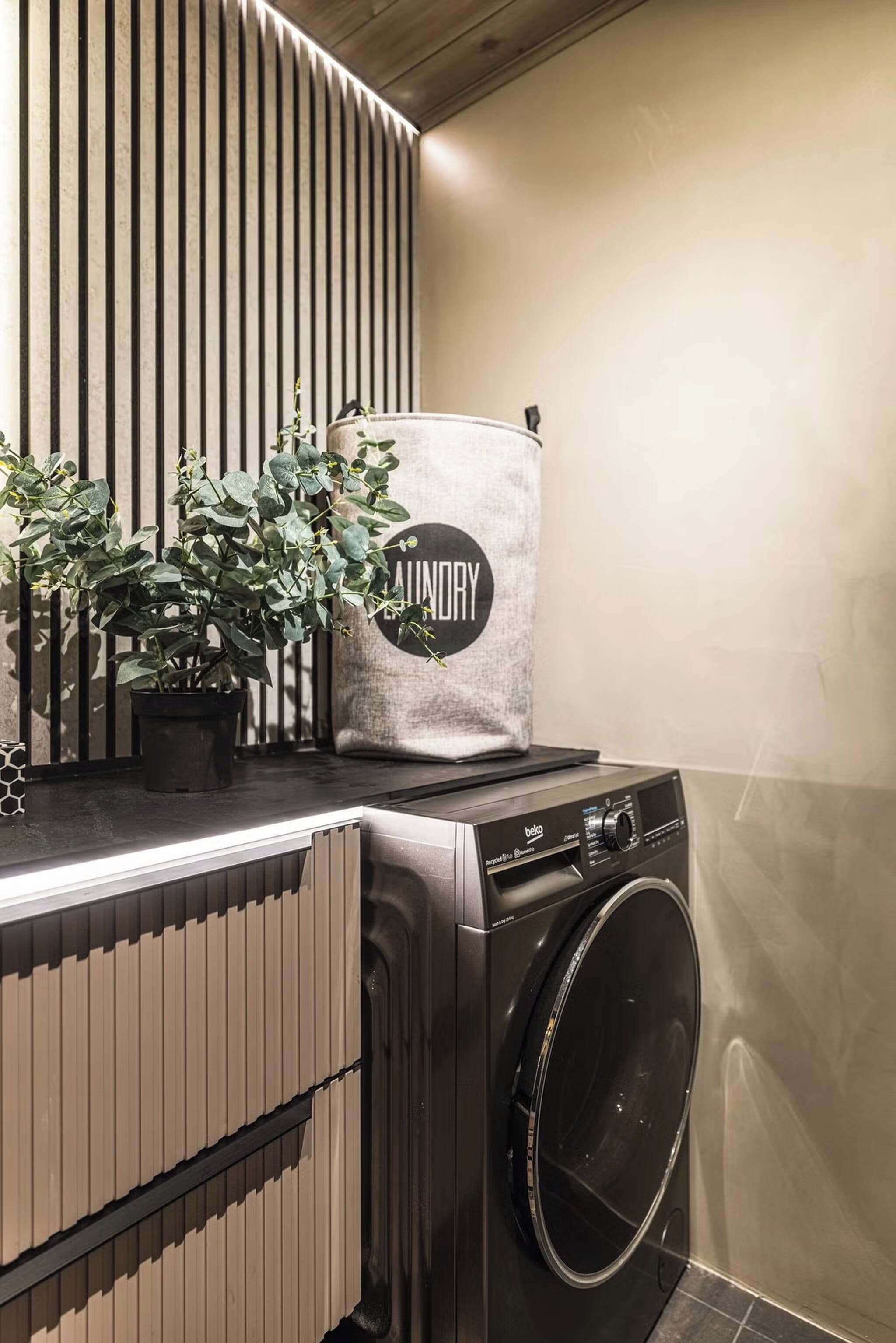 A modern laundry room with a built-in washer and dryer, a potted plant, and a vertical slatted wall.