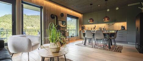 Un interior moderno con comedor, cocina y ventanas amplias que ofrecen vistas al exterior.