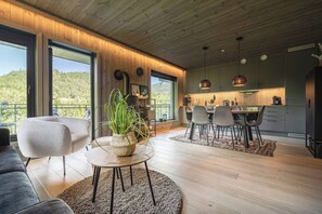 A modern interior with a dining area, kitchen, and large windows offering a view of the outdoors.