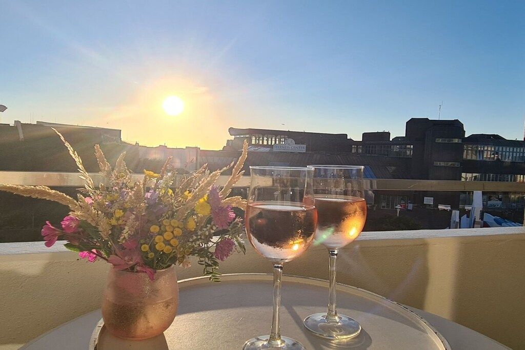 Une table avec deux verres de vin et un vase de fleurs sur un balcon donnant sur un paysage urbain.