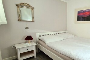 A bedroom with a single bed, a nightstand with a lamp, a wall-mounted mirror, and a framed picture. - Holiday apartment in Sylt with 2 bedrooms (Westerland\/Sylt)