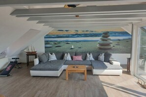 A modern living room with a sectional sofa, a wooden coffee table, and a large mural of a beach scene. - Casita Priscila || Waren\/Müritz (Waren\/Müritz)