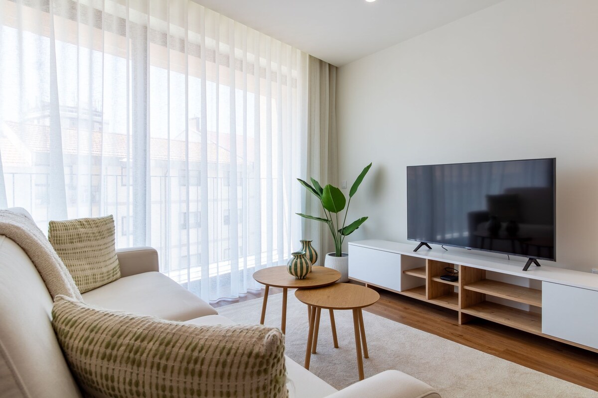 A modern living room with a sofa, a coffee table, a TV on a stand, and a plant.