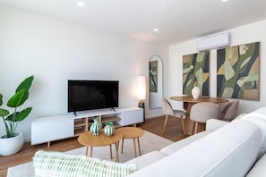 A modern living room with a flat-screen TV, a dining area with a table and chairs, and a large sofa. - Polacos Residence by LovelyStay (Vila Nova de Gaia)