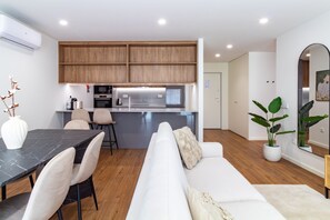 Una cocina moderna con armarios de madera, un comedor con una mesa de mármol y una sala de estar con un sofá blanco.