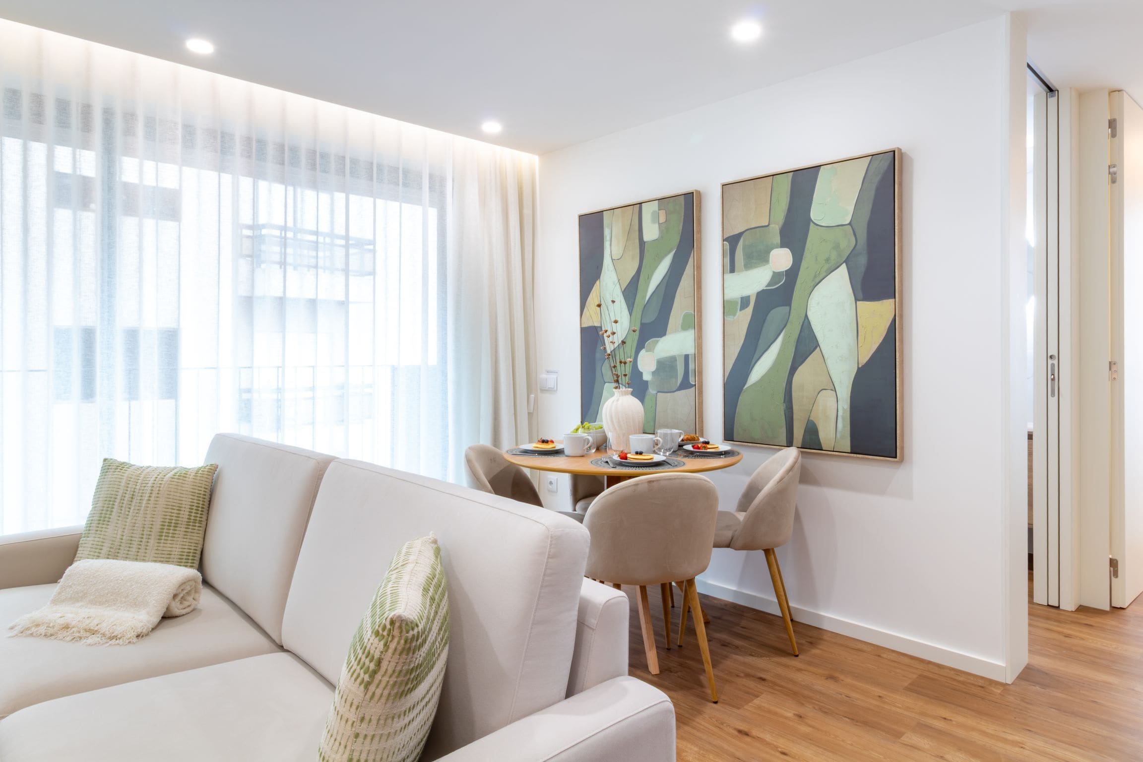Een moderne woonkamer met een bank, een eettafel met stoelen en abstracte schilderijen aan de muur.