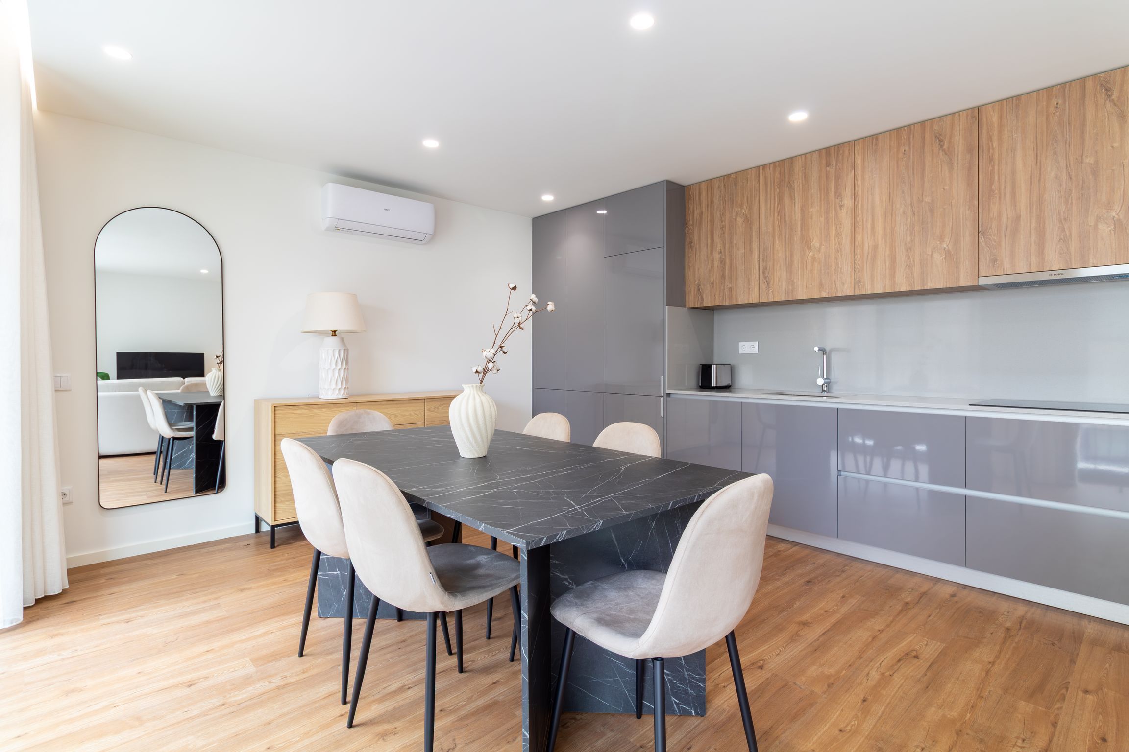 Een moderne keuken met grijze kastjes, een eettafel van zwart marmer en een vaas met takken.