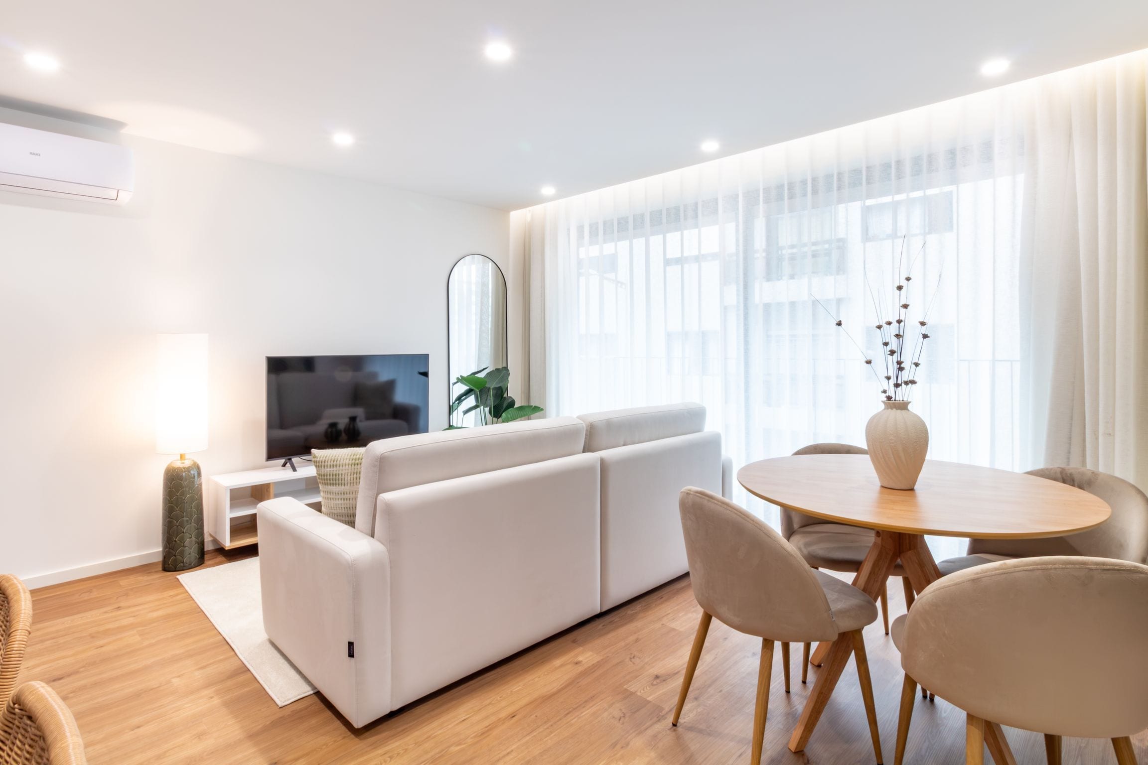 A modern living room with a sofa, TV, and a dining area with chairs and a table.