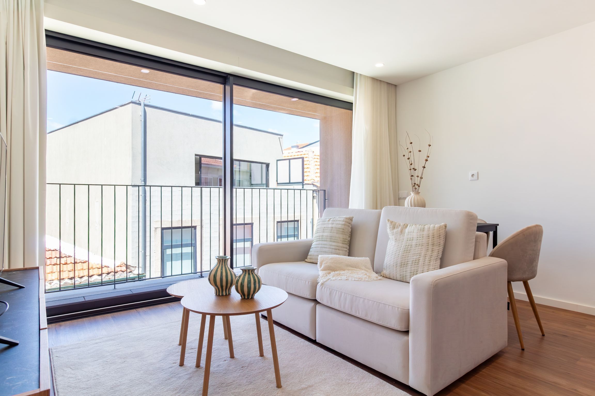 A modern living room with a sofa, two chairs, a small round table, and a vase with plants.