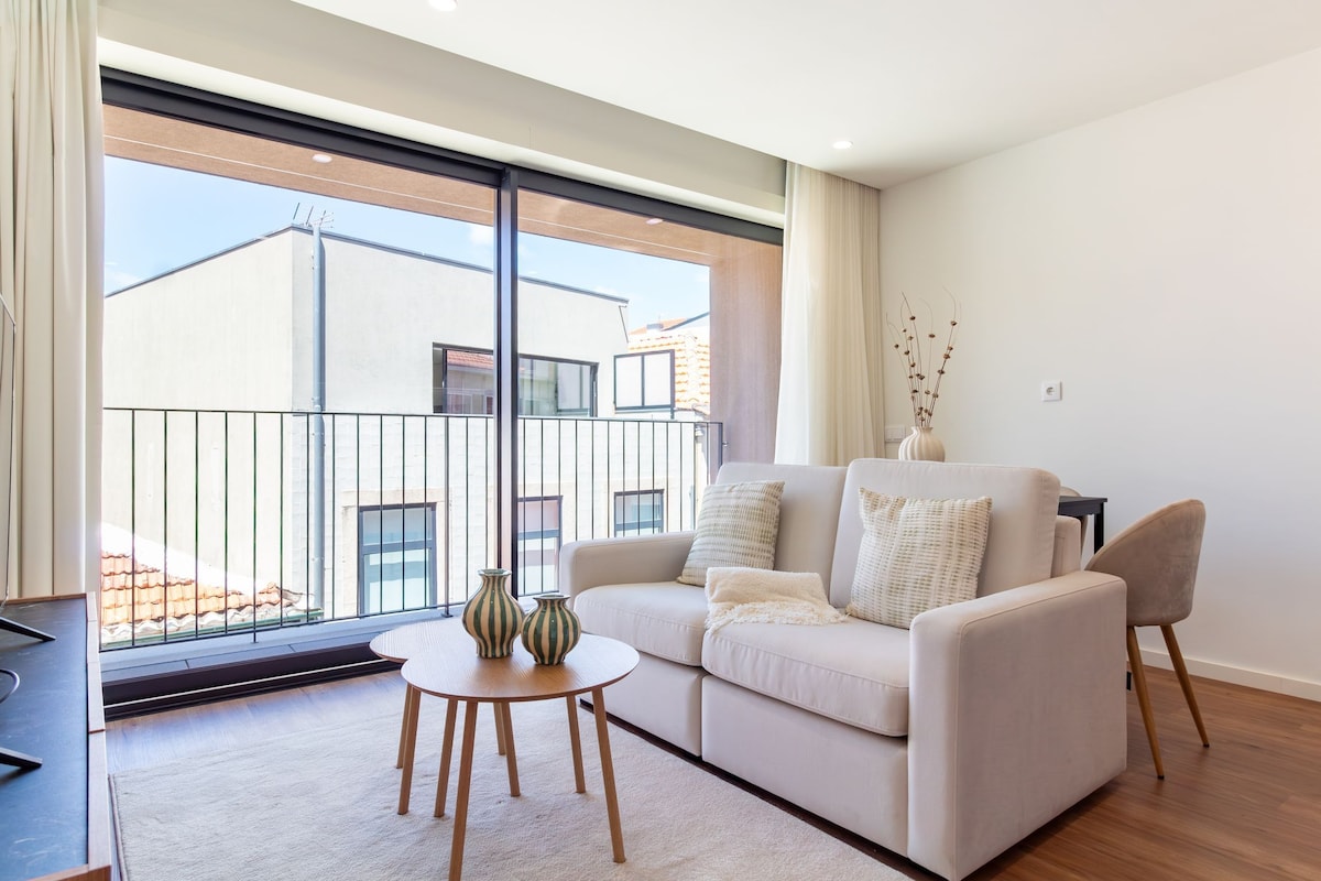 A modern living room with a sofa, two chairs, a small round table, and a vase with plants.