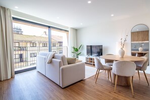 Uma sala de estar moderna com sofá, mesa de jantar, cadeiras, televisão e uma grande janela com vista para edifícios.