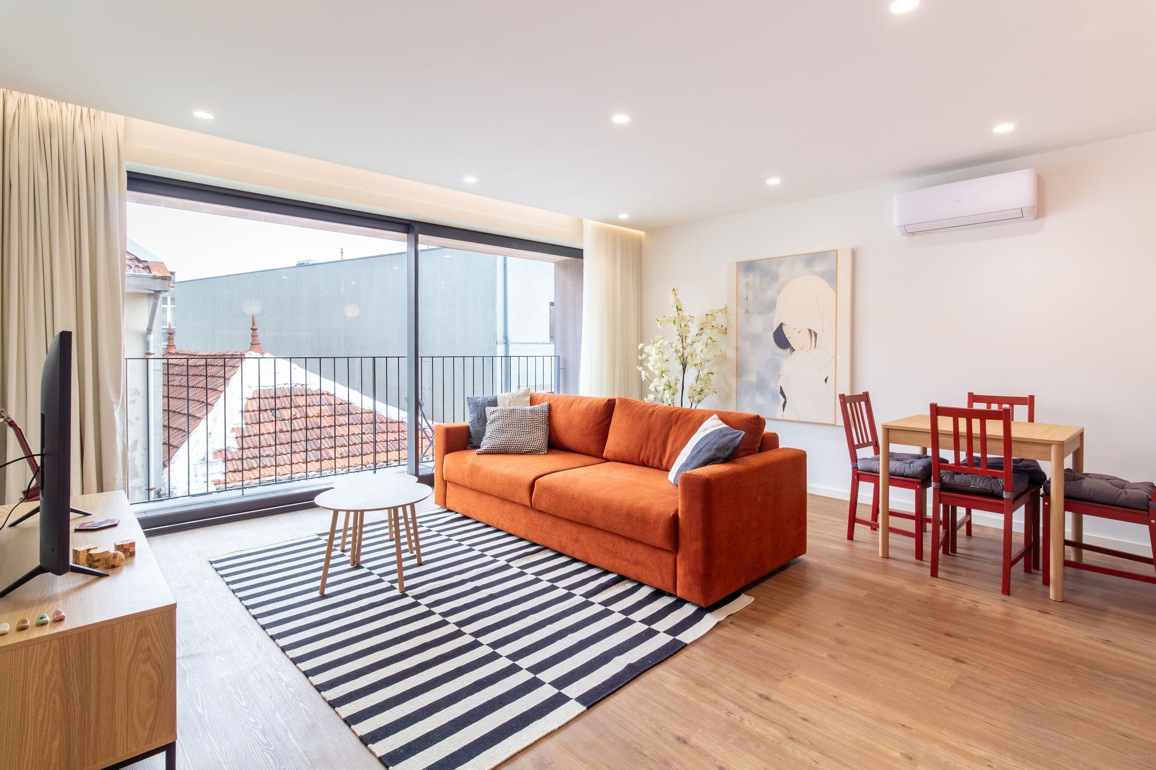 Een moderne woonkamer met een bank, eettafel, stoelen en een uitzicht op gebouwen door grote ramen.