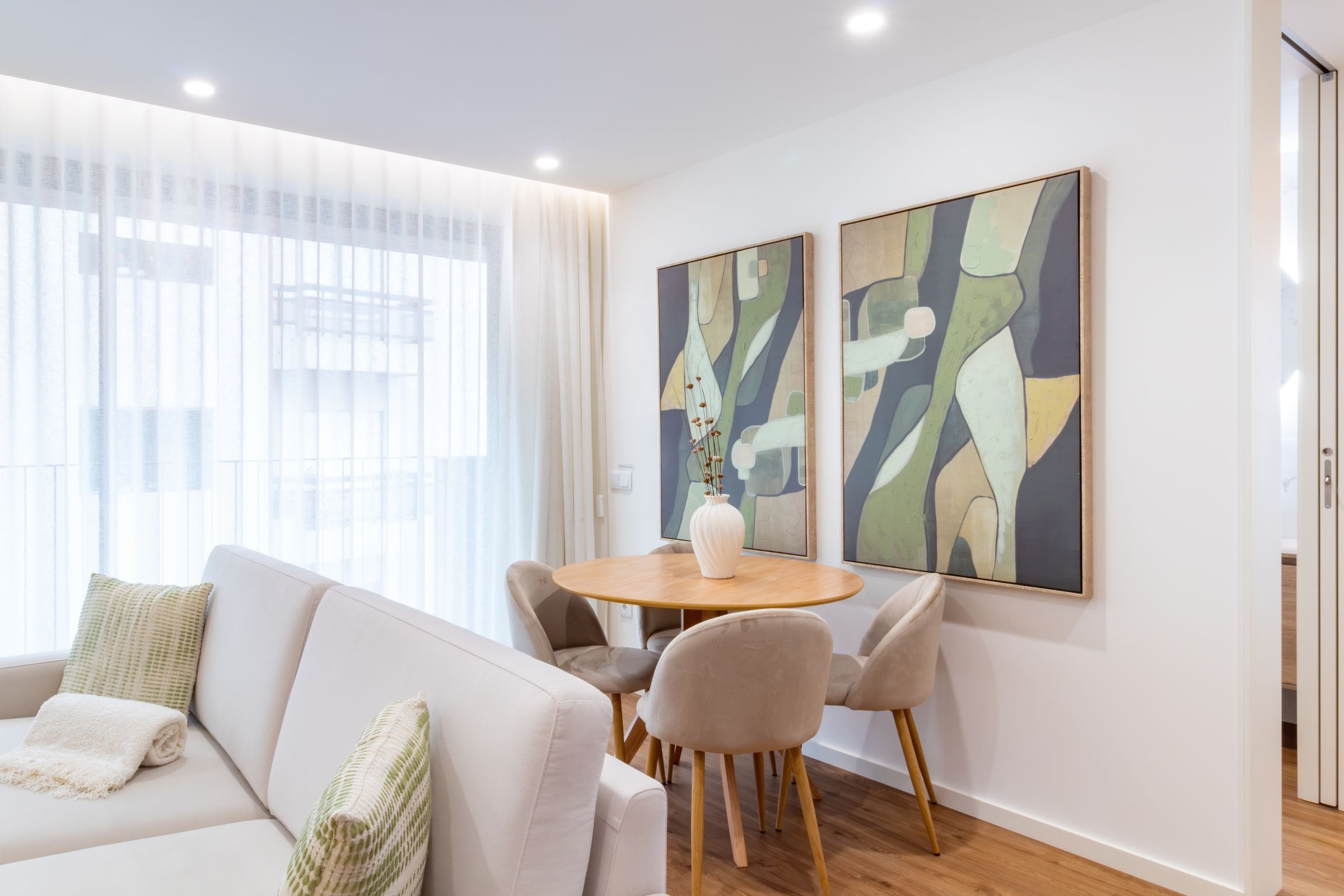 A modern living room with a sofa, chairs, a round table, and abstract paintings on the wall.