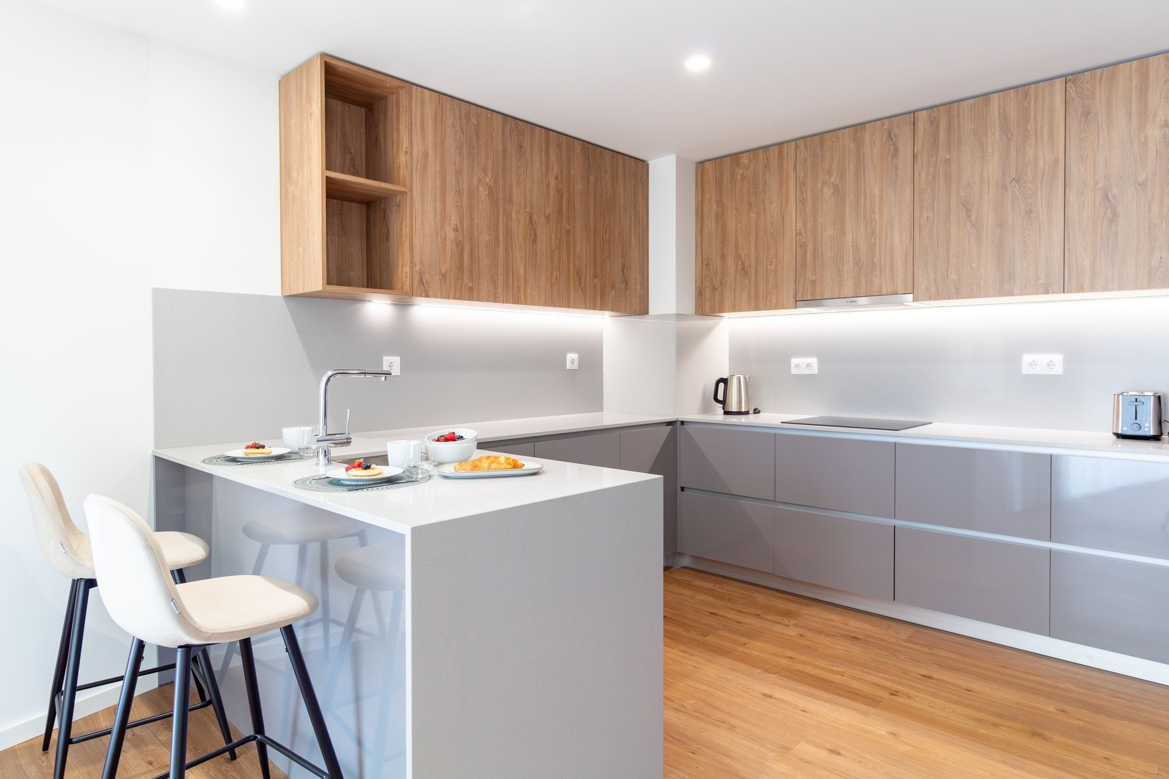 Een moderne keuken met een centraal eiland, barkrukken, houten kastjes en een inbouwoven.