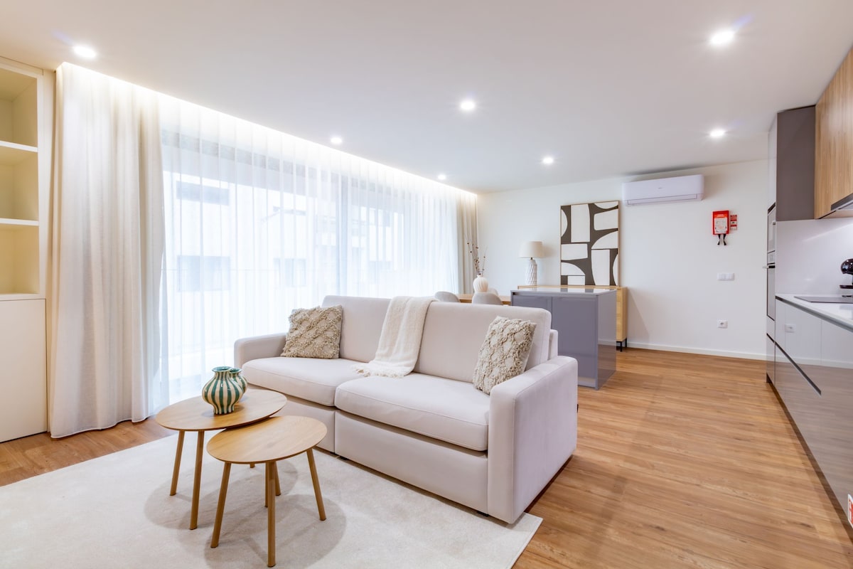 A modern living room with a sofa, two small tables, and a kitchen area in the background.