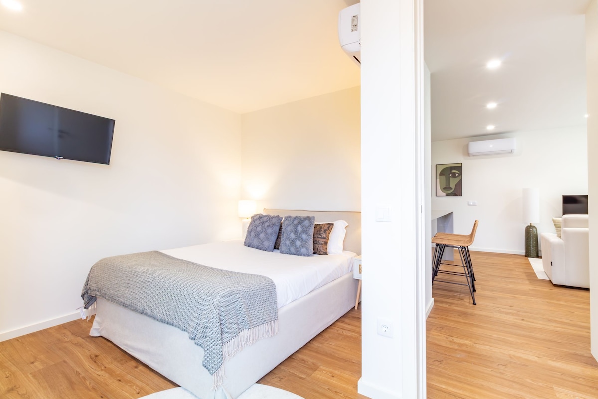 A modern bedroom with a bed, a flat-screen TV, and a small seating area with a chair and a table.