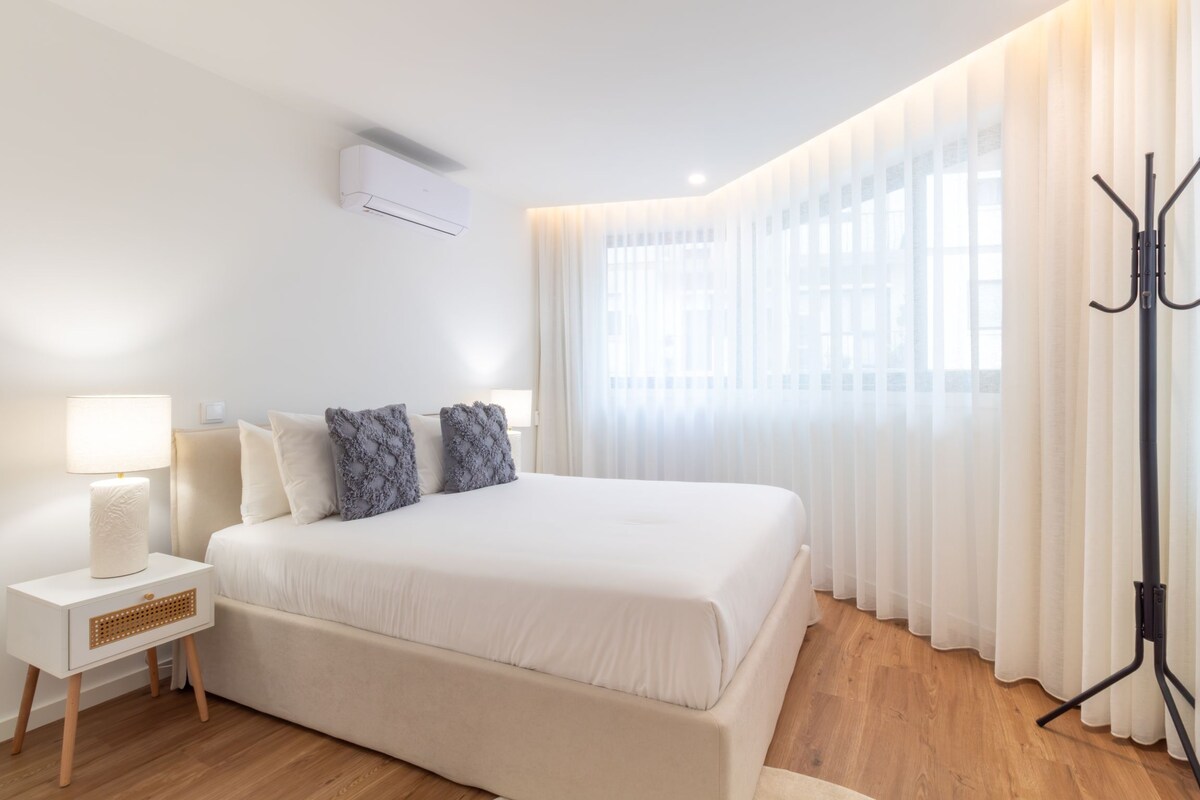 A bedroom with a bed, bedside table, lamp, and a window with curtains.