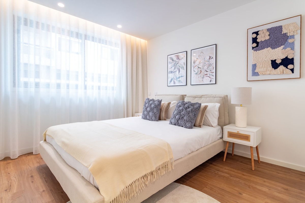 A bedroom with a large bed, a bedside table with a lamp, and artwork on the wall.