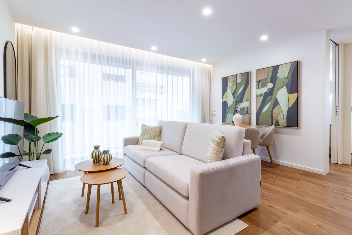 A modern living room with a sofa, a coffee table, and a TV. There are abstract paintings on the wall and a plant on the side.