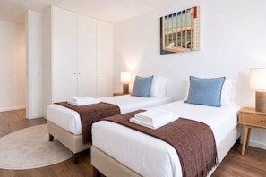 Habitación de hotel con dos camas, un armario, un cuadro y una mesita de noche con lámpara.
