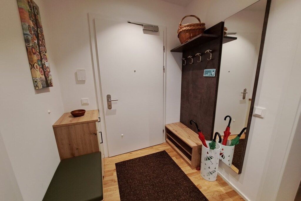 A hallway with a wooden bench, a door, a mirror, and a wall-mounted basket.