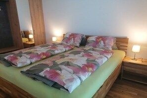 A double bed with floral bedding, wooden headboard, bedside tables with lamps, and a wooden wardrobe. - Apartment with 1 bedroom (Annenheim am Ossiachersee)