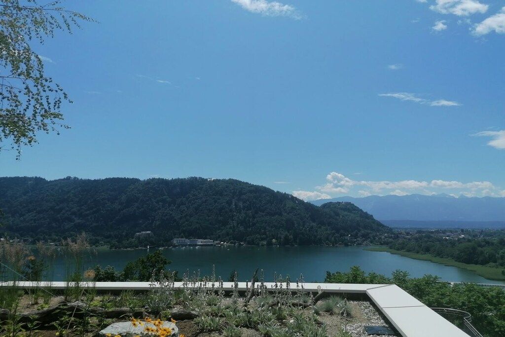 A lakeside view with a mountain backdrop, a clear sky, and a distant town.