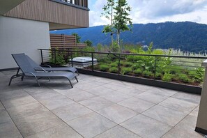 A balcony with two lounge chairs, a small table, and a view of a mountainous landscape. - Apartment with 1 bedroom (Annenheim am Ossiachersee)