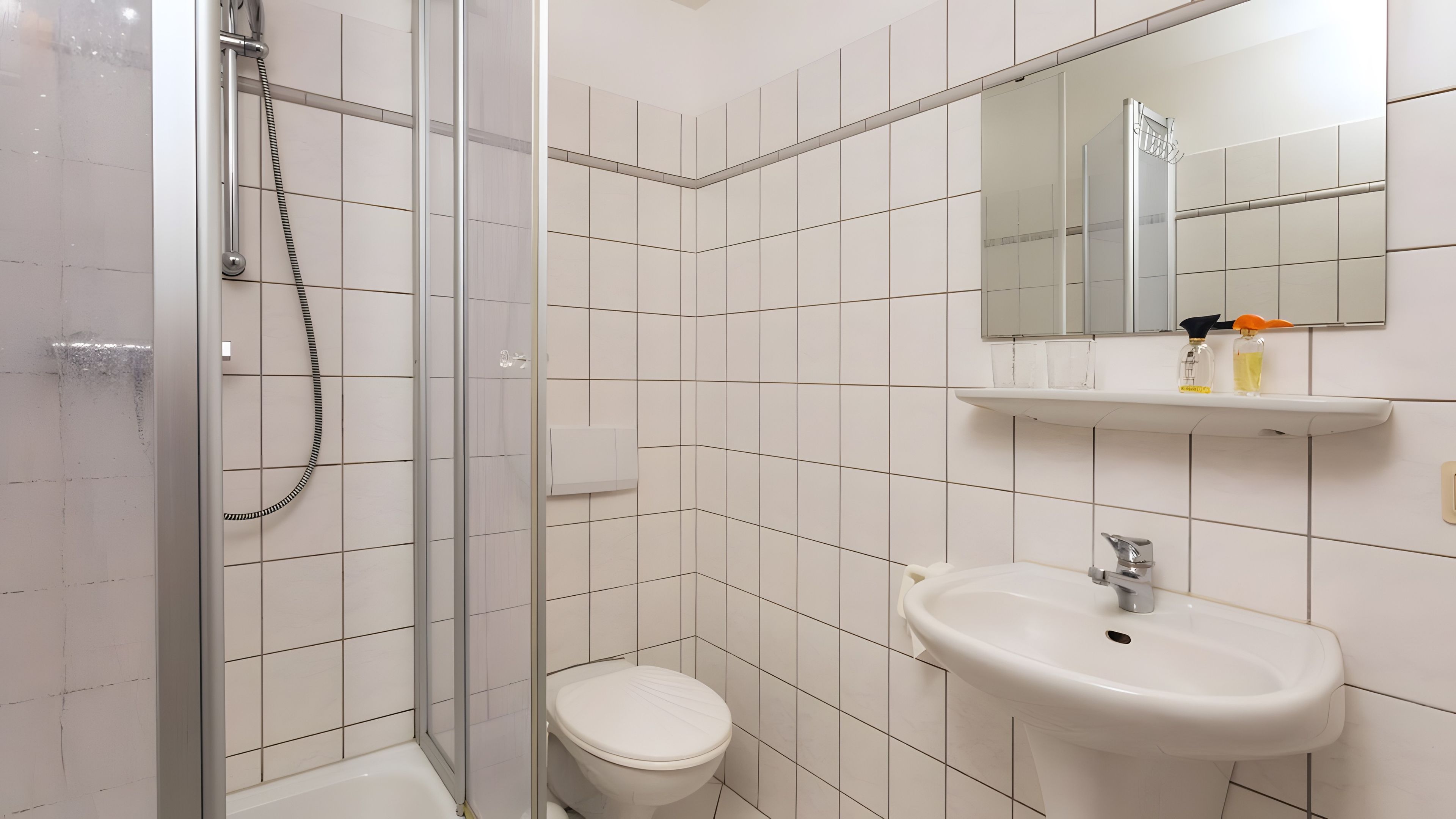 Ein Badezimmer mit einer Duschkabine, einem weißen Waschbecken und einem Spiegel darüber.