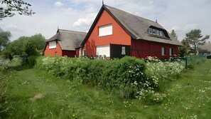 En röd byggnad med ett halmtak, omgiven av grönska och vita blommor.