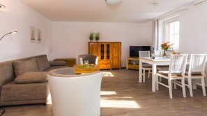 Ein Wohnzimmer mit einer Couch, einem Esstisch mit Stühlen, einer Holzkommode und einem Fernseher.