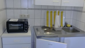 Ett litet kök med en svart brödrost, ett vitt kylskåp, en diskho och en handduksställning med gula ränder.