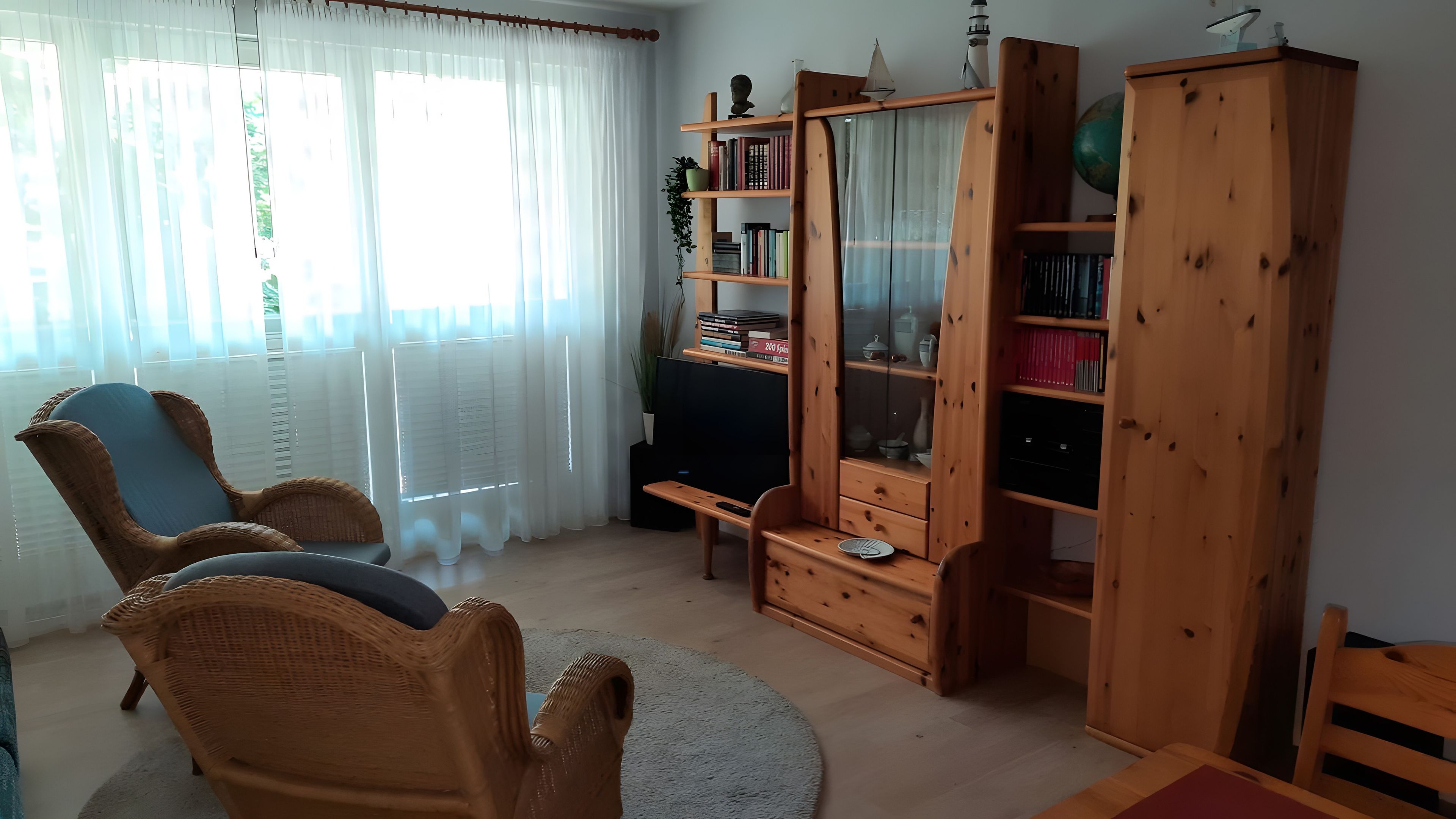 Ein Wohnzimmer mit Korbstühlen, einem Holzschrank mit Büchern, einem Fernseher und einem Globus.