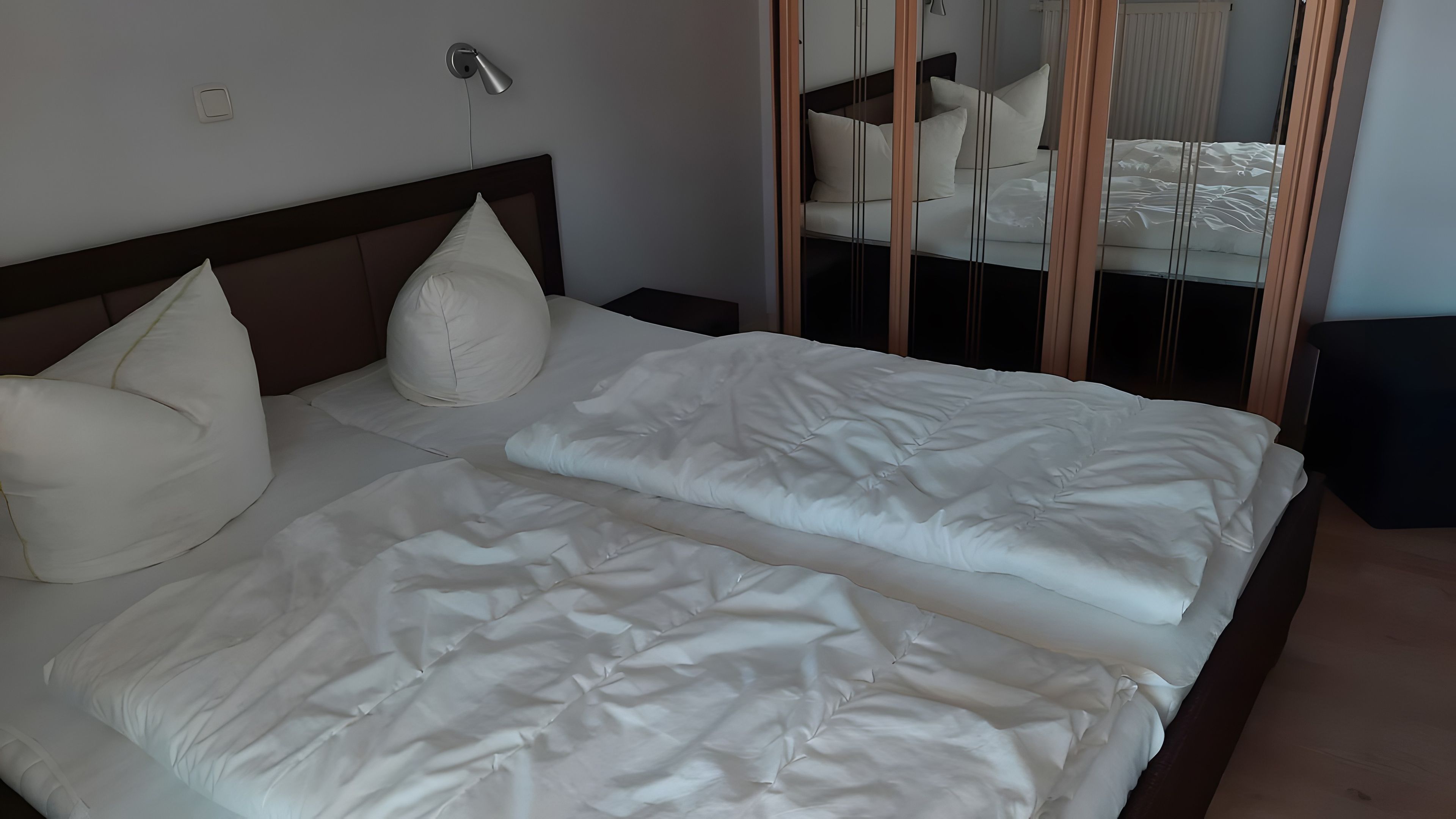 Ein Doppelbett mit weißer Bettwäsche und zwei Kissen, ein Nachttisch und eine Wandlampe.