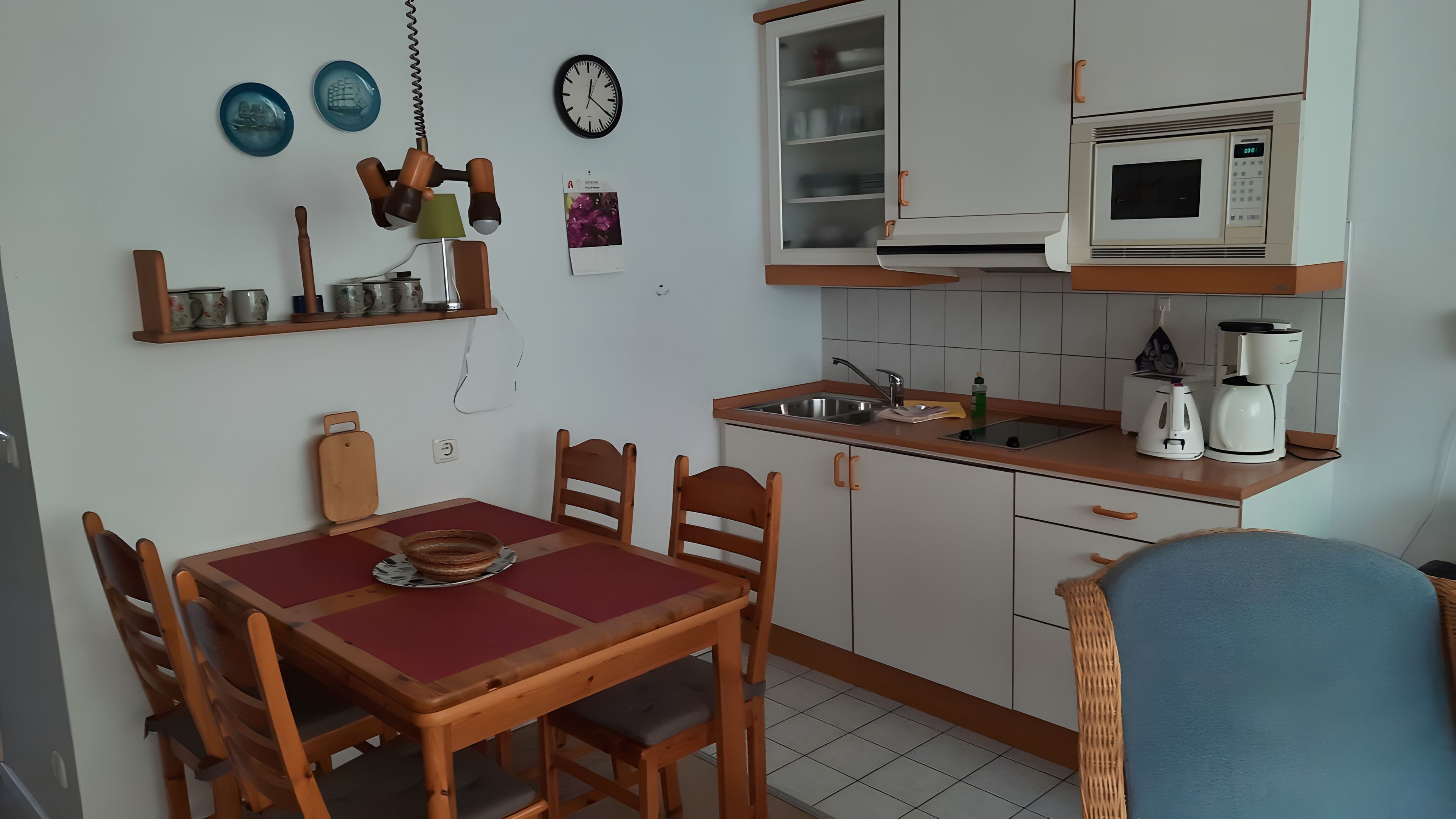 Eine kleine Küche mit Esstisch, Stühlen, einer Mikrowelle, einer Kaffeemaschine und einem Regal mit Dekorationsplatten.