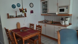 Una cuina compacta amb taula de menjador, caires, microones, cafetera i una estant amb plats decoratius.