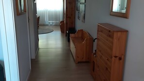 Passadís amb mobles de fusta, com ara un aparador i una banca, que condueix a una habitació amb finestra i cortines.