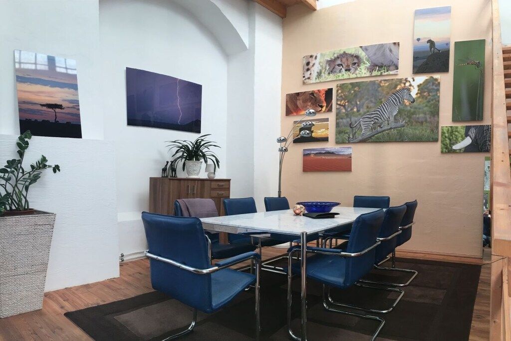 A dining area with a white table, blue chairs, and artwork on the walls.