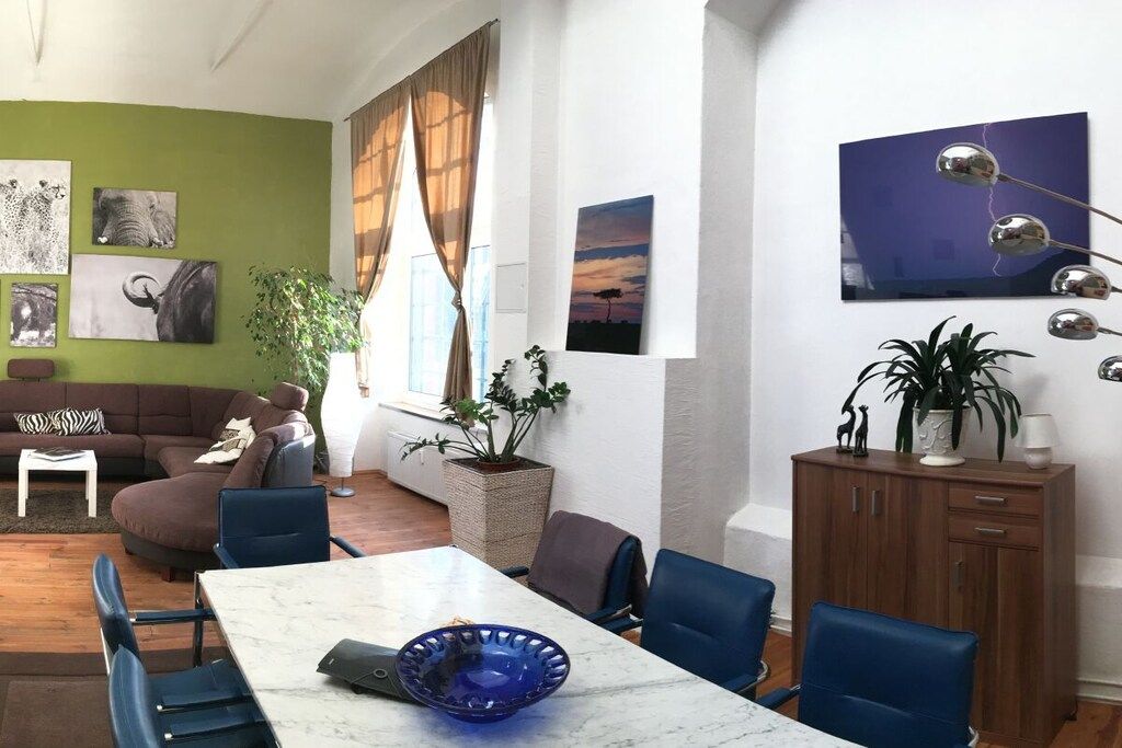 A modern living room with a sectional sofa, a dining table with chairs, and a large window with curtains.