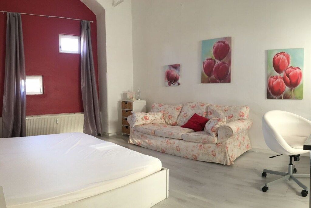 A bedroom with a bed, a sofa, a chair, and artwork on the wall.