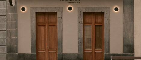 Facciata di un edificio con due porte in legno, un cartello che indica 'TRIANA 54 Restaurante' e una panchina a destra.