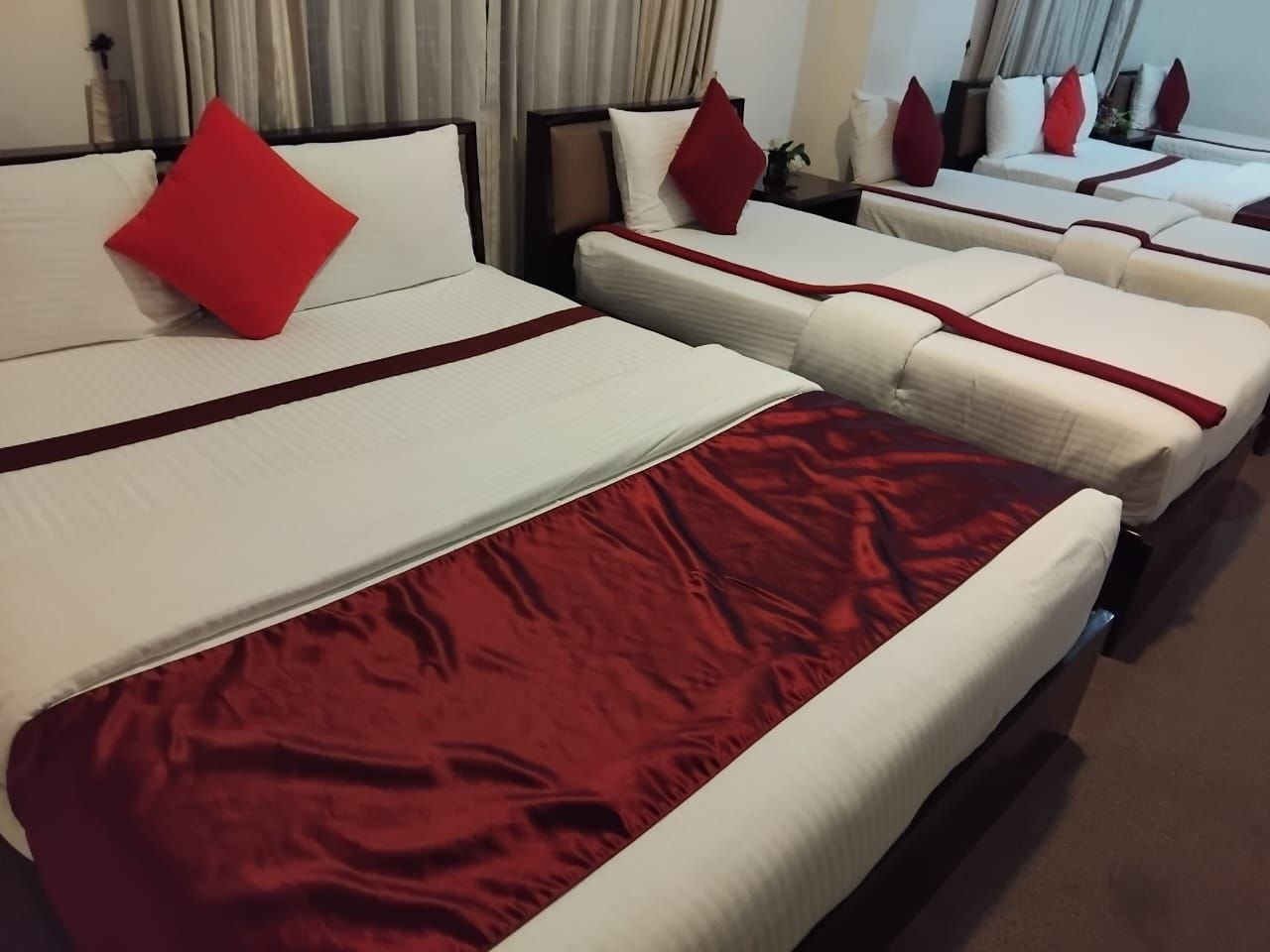 A hotel room with two beds, each with a red accent pillow and a white bedspread.