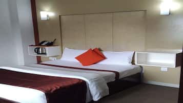 A hotel room with a bed, a bedside table with a phone and a kettle, and a wall-mounted light fixture.