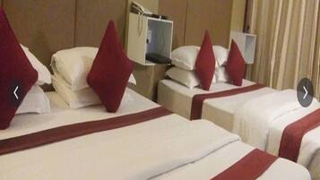 A hotel room with three beds, each with white bedding and red accents, and a television on a stand.