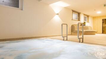 A room with a large, white, heated floor, a metal ladder, and a stone bench.