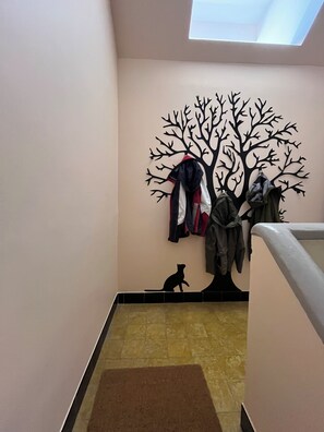 Un pasillo con un perchero, un adorno de árbol montado en la pared, una silueta de gato y un suelo de baldosas.