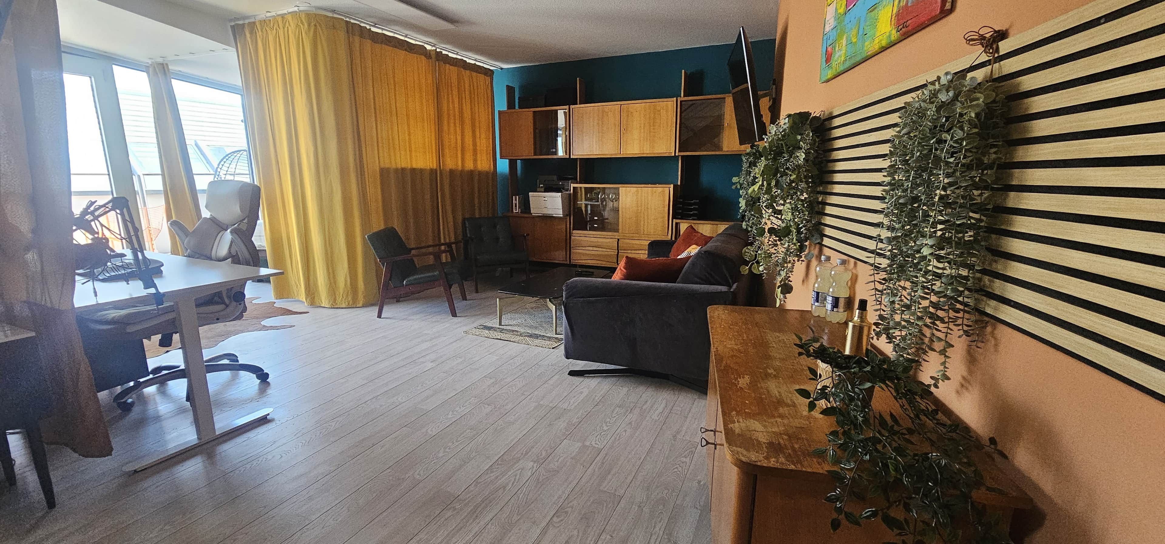 Ein Wohnzimmer mit Schreibtisch, Sesseln, einer Couch und einem Fernseher.