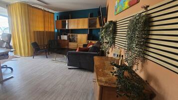 Ein Wohnzimmer mit Schreibtisch, Sesseln, einer Couch und einem Fernseher.
